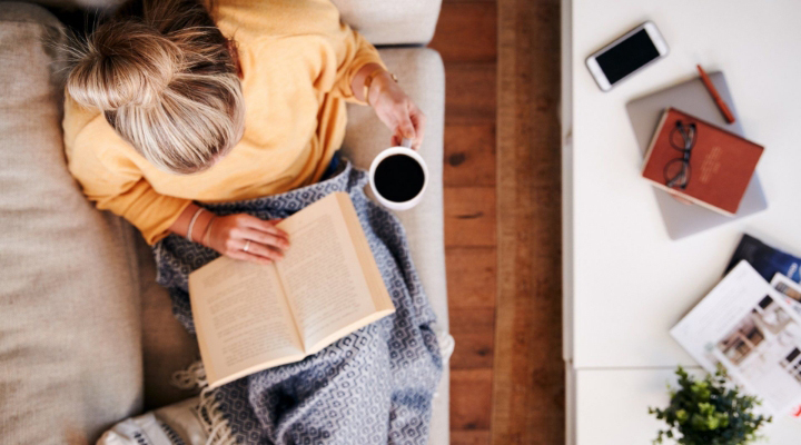 a woman drinking coffee on the couch reading